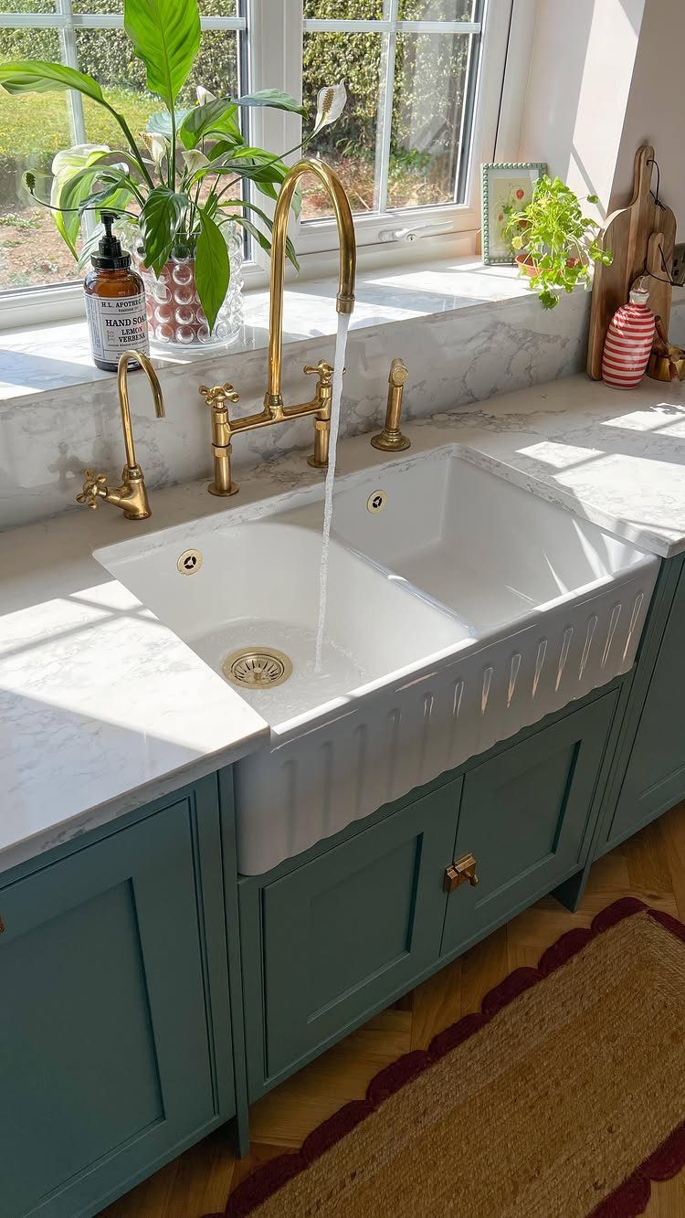 15 Ranch Style House Kitchen Remodel Ideas, Retro to Modern 2 White double-bowl farmhouse sink with gold faucets and teal cabinets under a window.