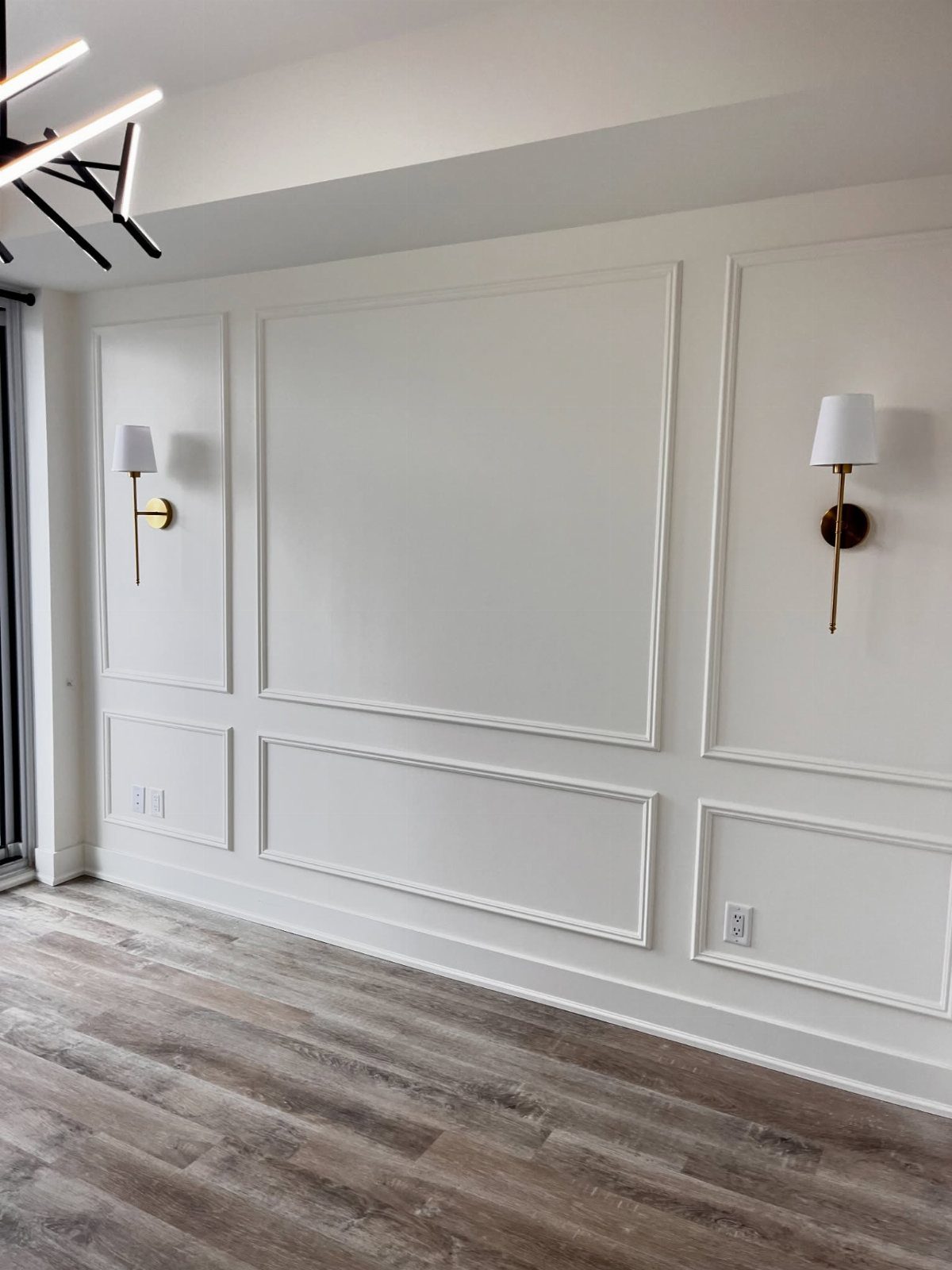 17 Remodeling Old House Ideas for Kitchens, Baths, Offices 14 White wall with decorative molding panels and two gold wall sconces above wood flooring.