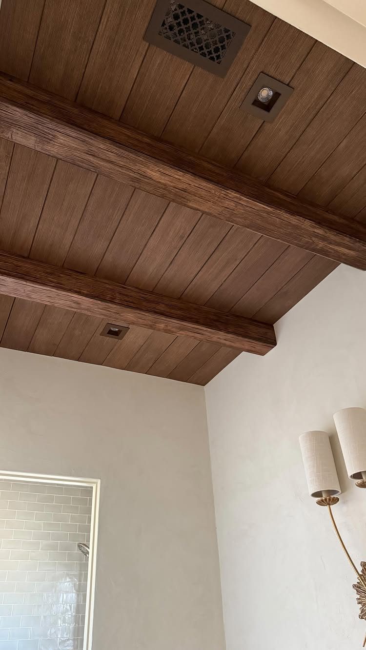 Dark brown wooden plank ceiling with heavy rustic beams and white walls.