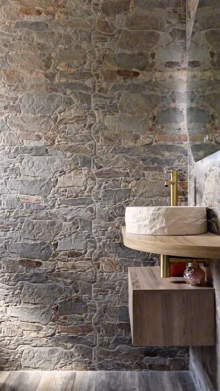 Natural stone wall and carved stone vessel sink in a rustic bathroom setting.
