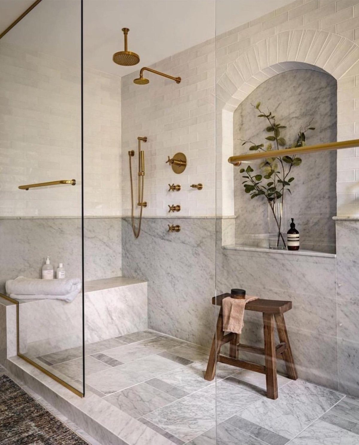 Bathroom shower with two-tone walls featuring white tiles above grey marble wainscoting.