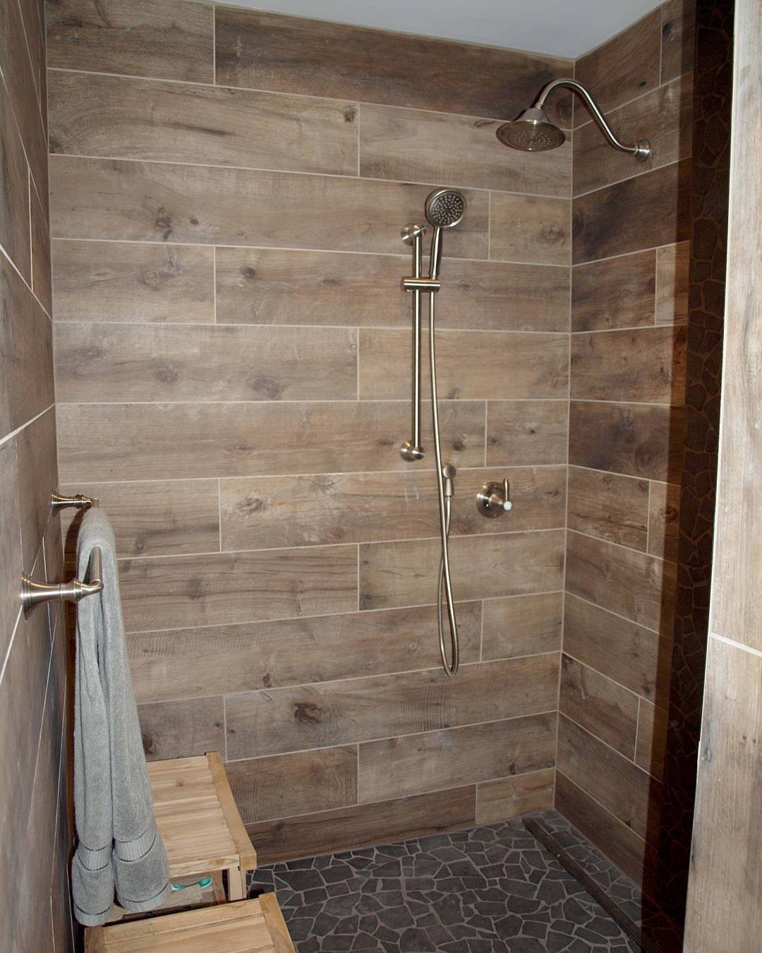 Walk-in shower with brown wood-look wall tiles and dark pebble stone flooring.