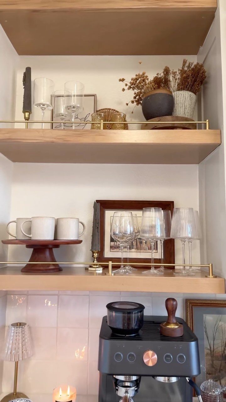 Wooden floating shelves above a black espresso machine with glassware and dried flowers.