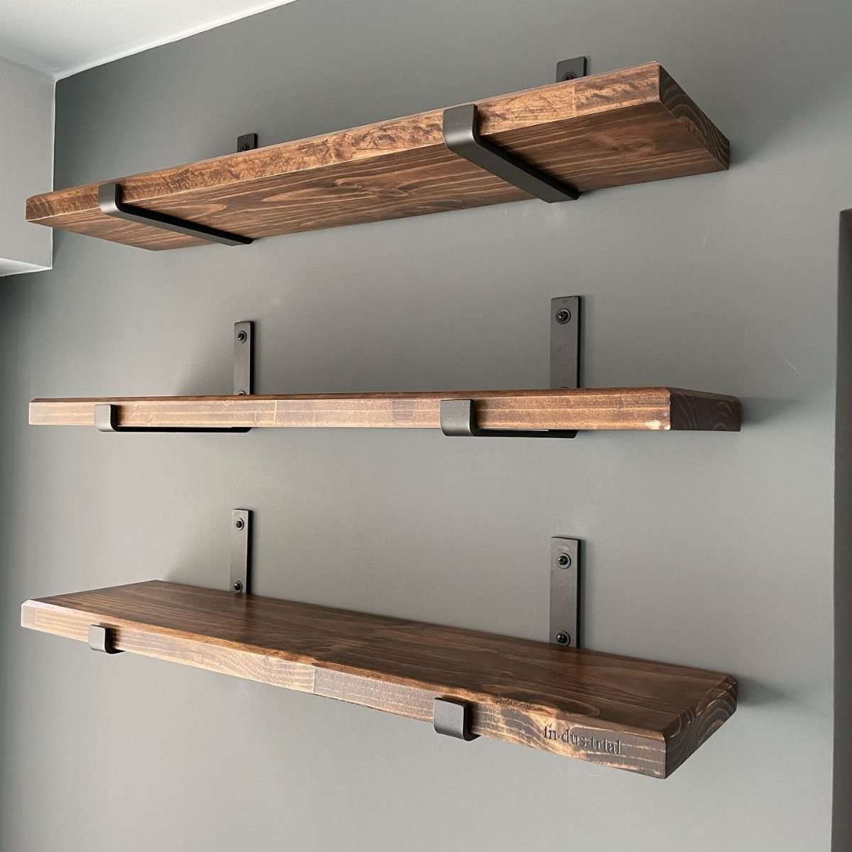 Dark wooden shelves with black metal industrial brackets mounted on a grey wall.