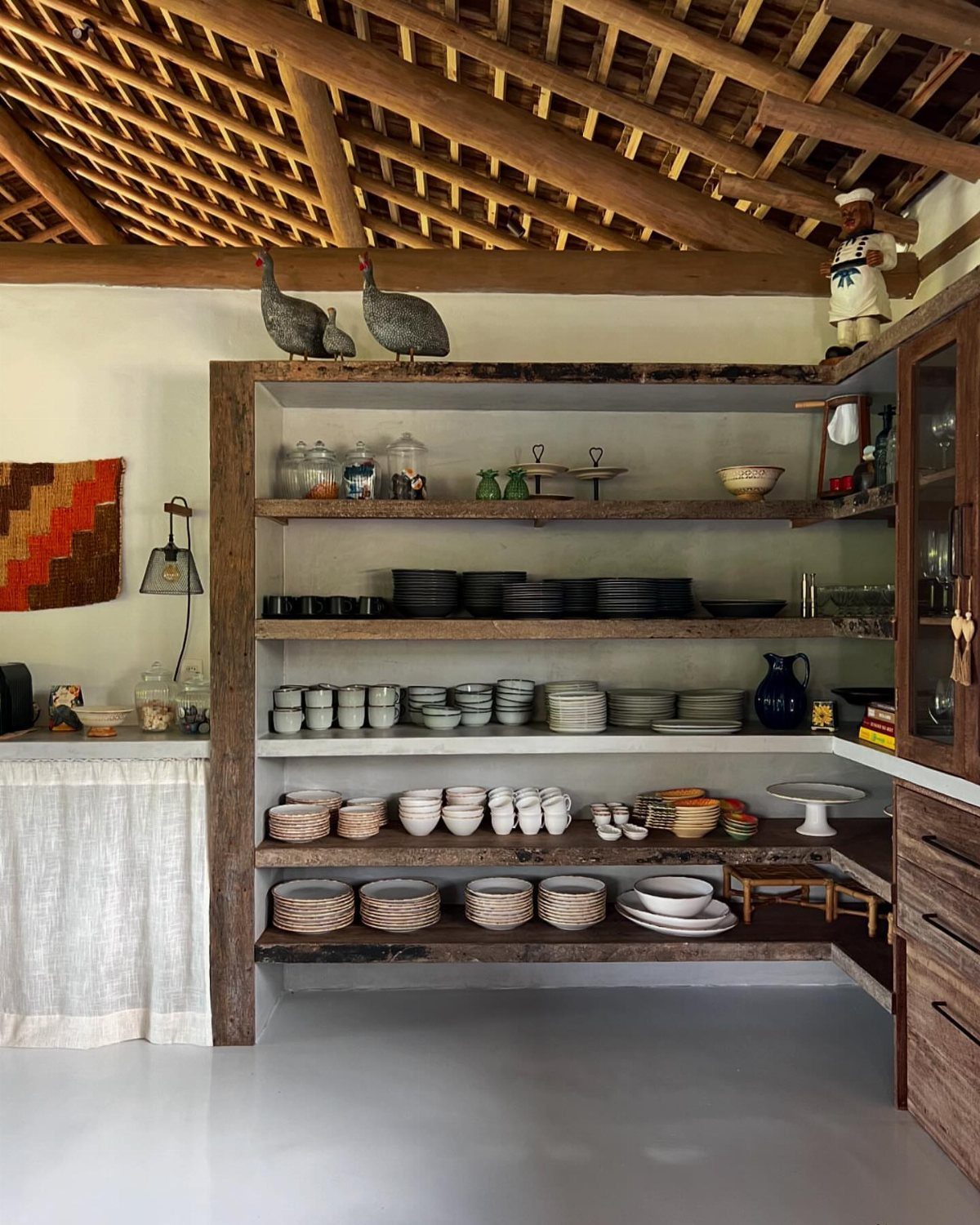 Wooden open shelves built into a kitchen niche holding various ceramic dishes and bowls