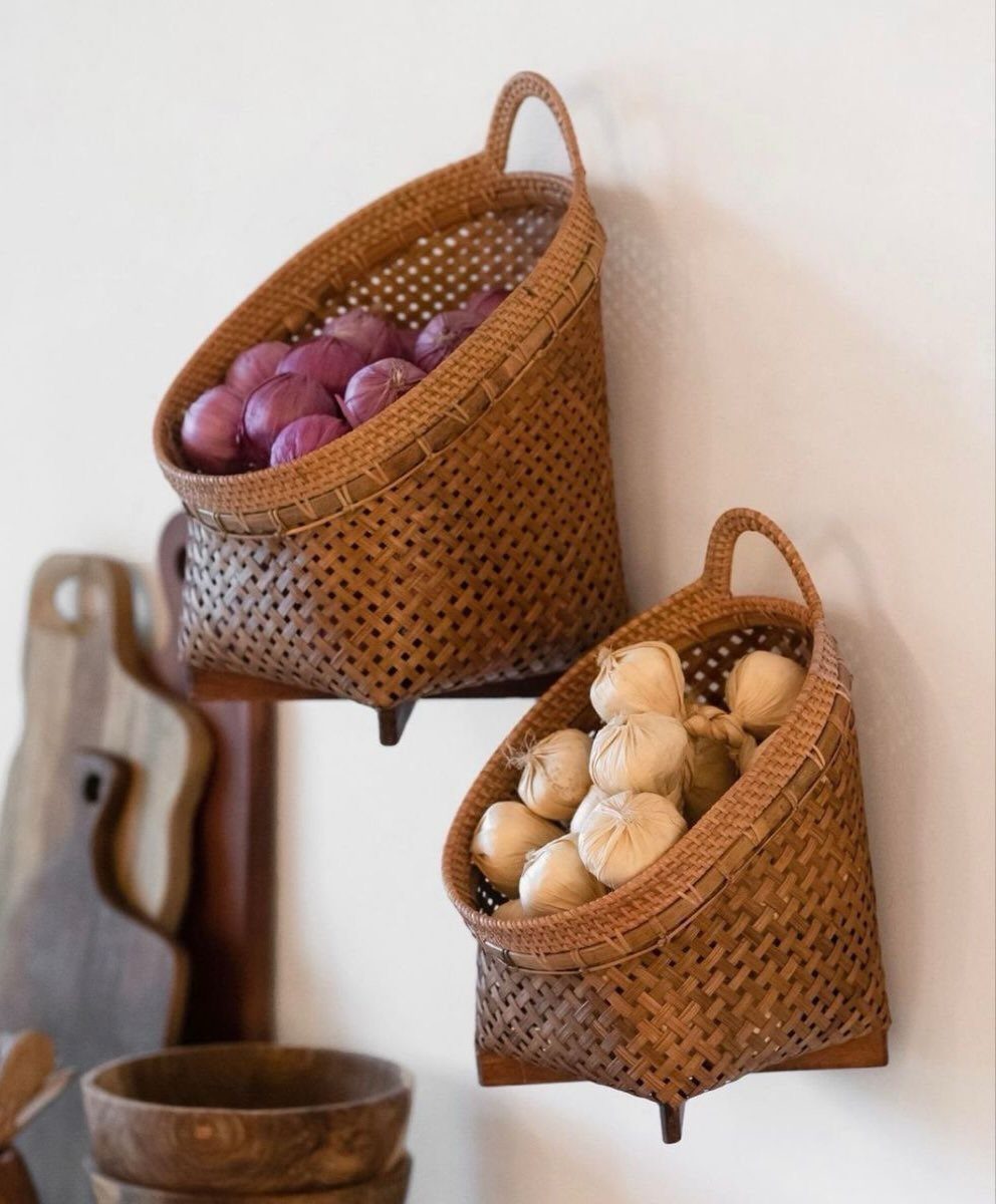 Two woven water-hyacinth wall baskets holding red onions and garlic on a white wall