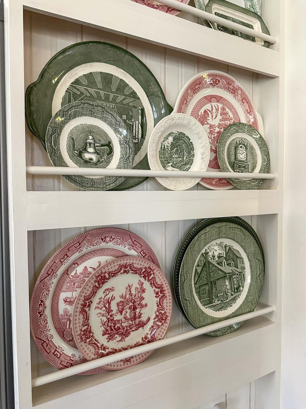 White rustic kitchen shelves displaying decorative red and green ceramic plates.