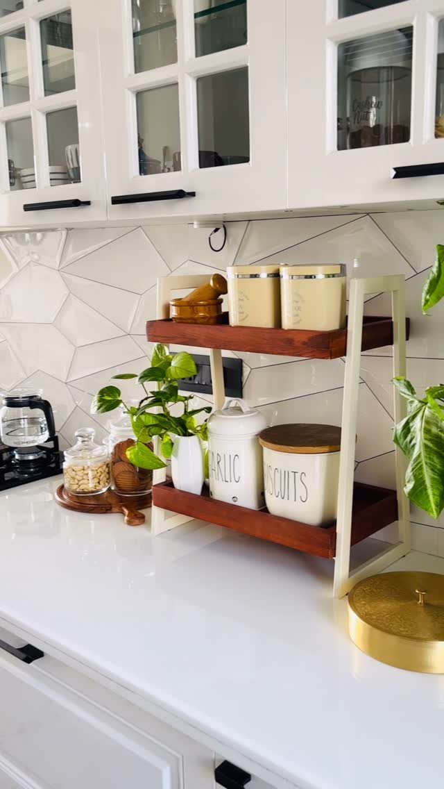 Two-tier wooden and metal countertop shelf holding kitchen canisters and spice jars.