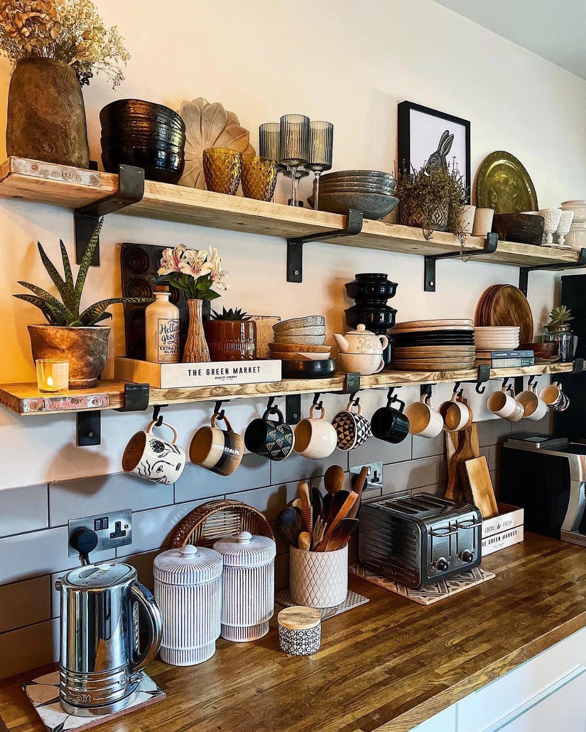 Rustic wooden kitchen shelves holding glassware and plants above a wooden countertop.