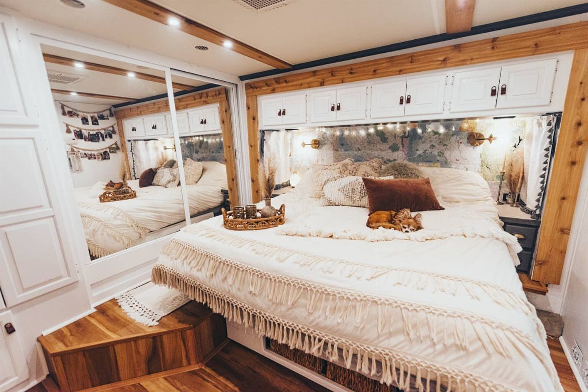 RV bedroom with cream fringed bedding, white overhead cabinets, and mirrored closet doors.