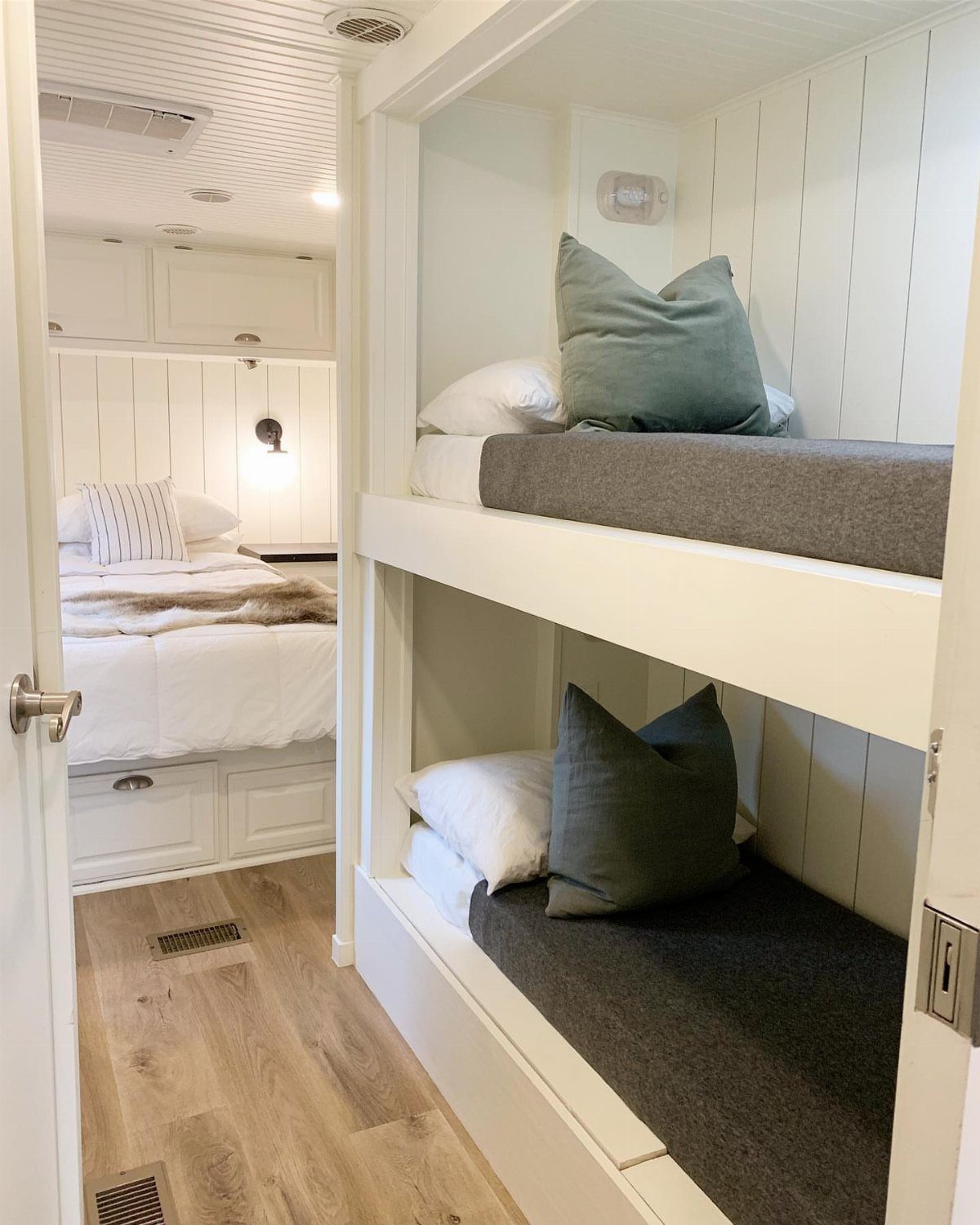 White built-in bunk beds with grey mattresses and teal pillows in an RV.
