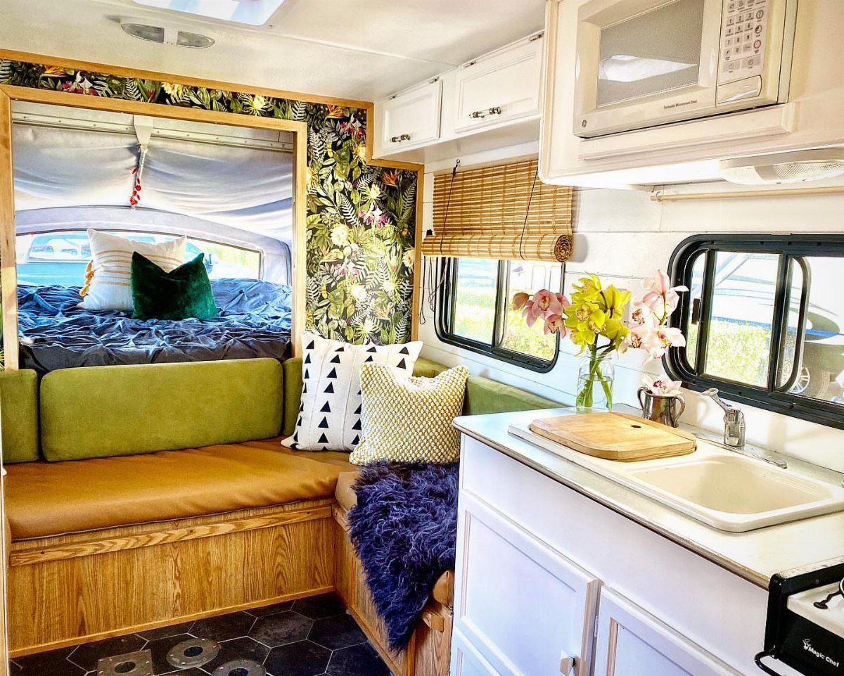 RV interior with a tan seating nook, white kitchen, and floral accent wall.