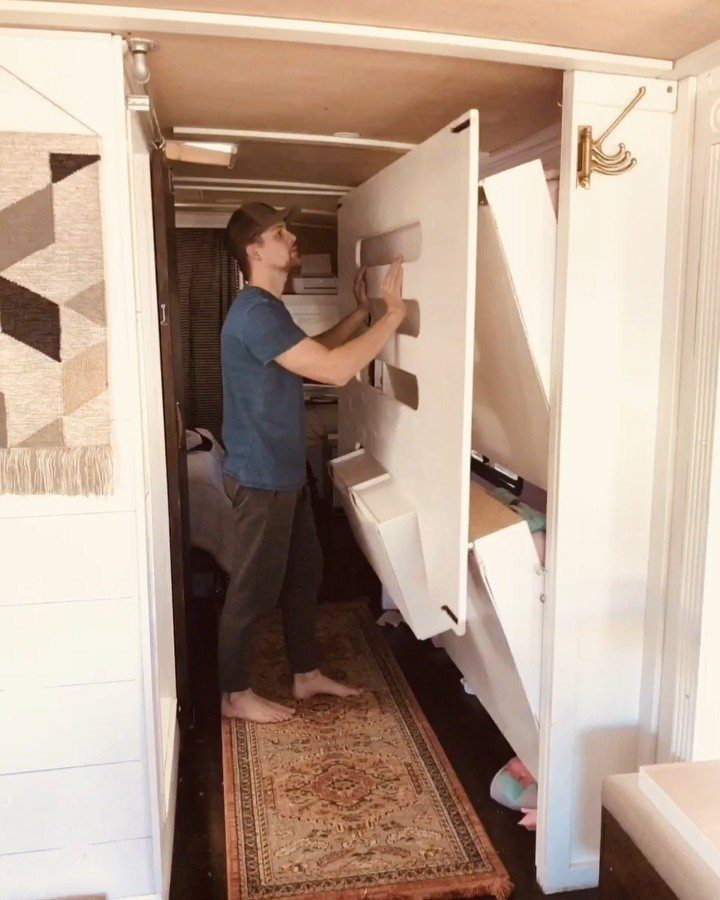 Man adjusting a white folding bed inside a remodeled RV bedroom with patterned rugs.