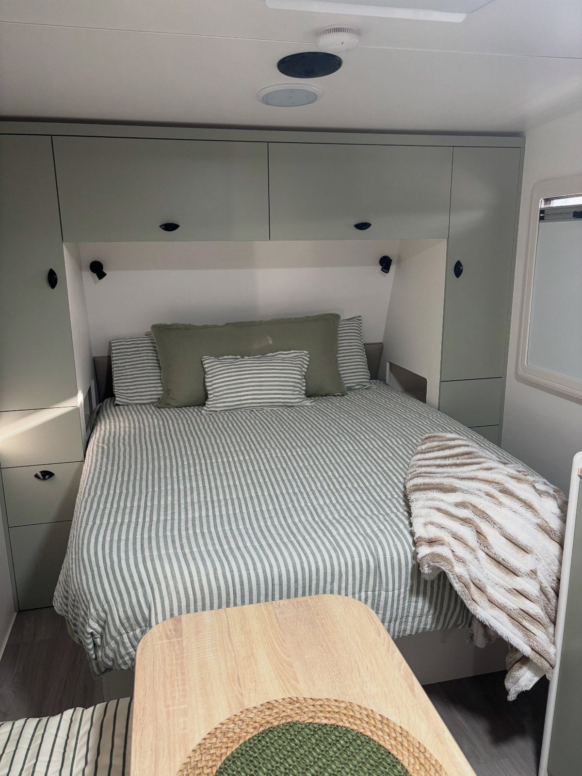 Bed with striped bedding and green pillows inside a light green RV bedroom