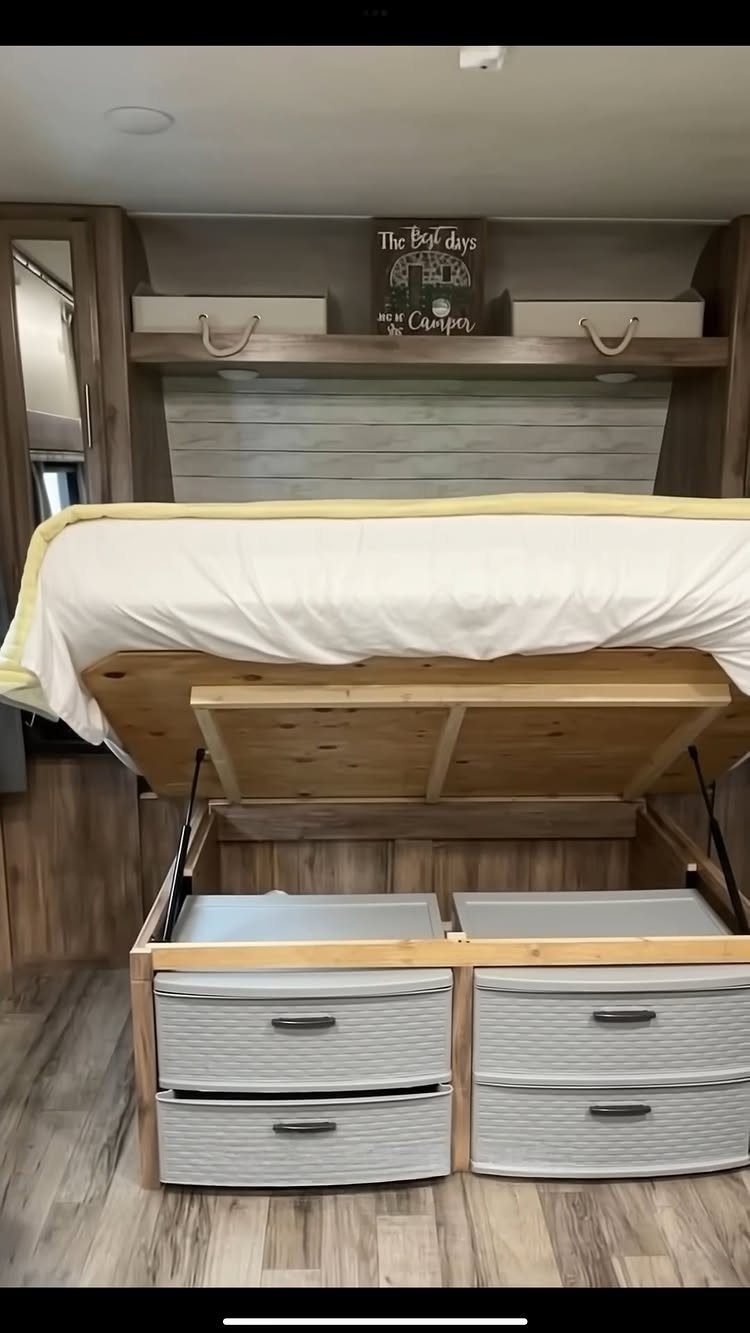 RV bedroom with a lift-up bed platform revealing storage bins underneath wood-paneled walls.