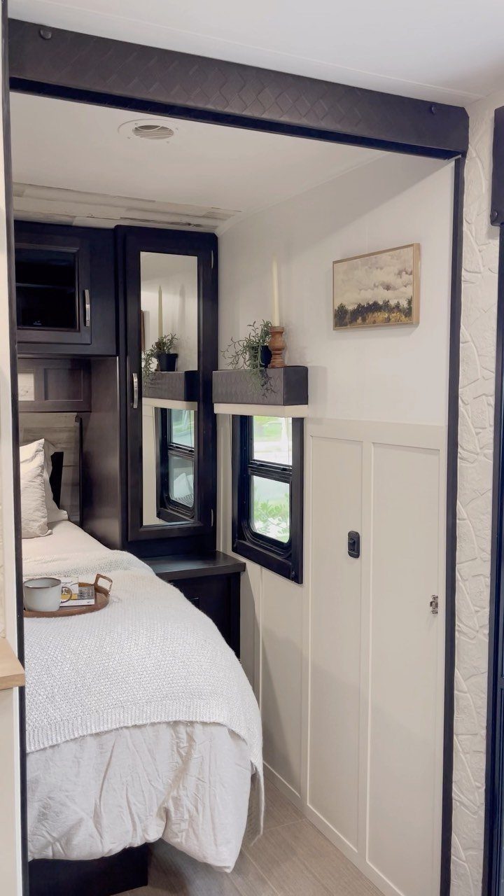 RV bedroom with white bedding, navy blue cabinets, and a wall mirror.