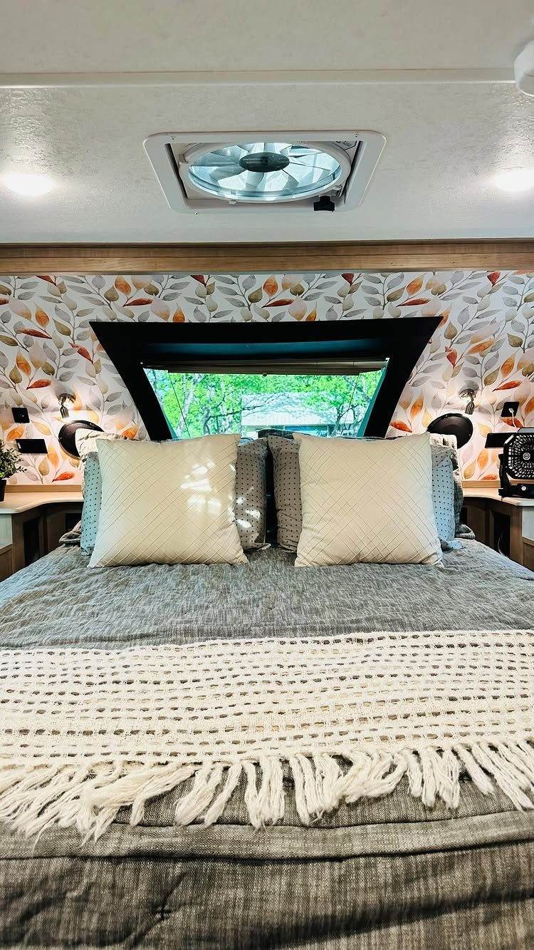 Bed with grey linens and leaf-patterned wallpaper inside a remodeled RV bedroom
