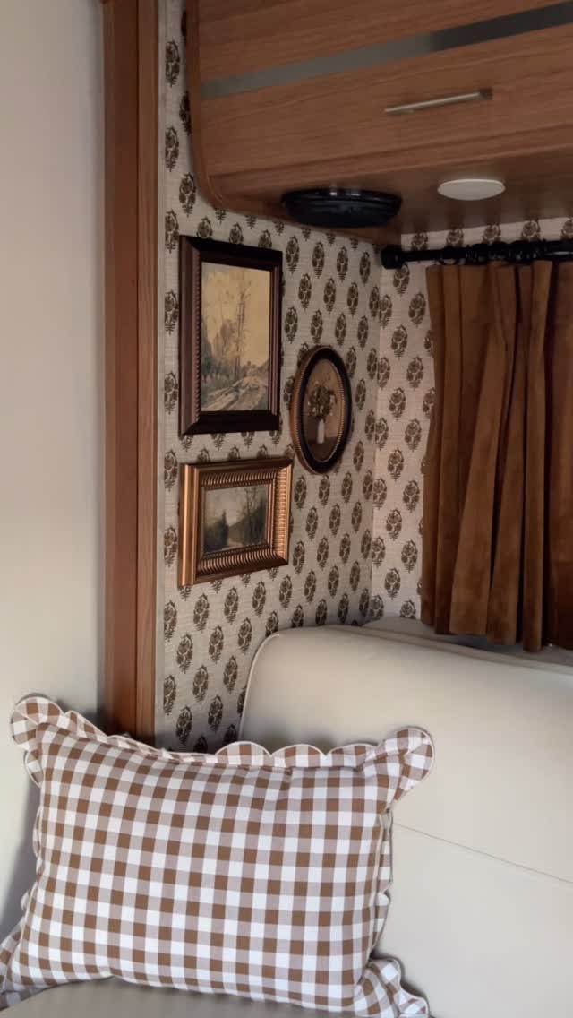 Patterned wallpaper on an RV wall with framed art and a checkered pillow.