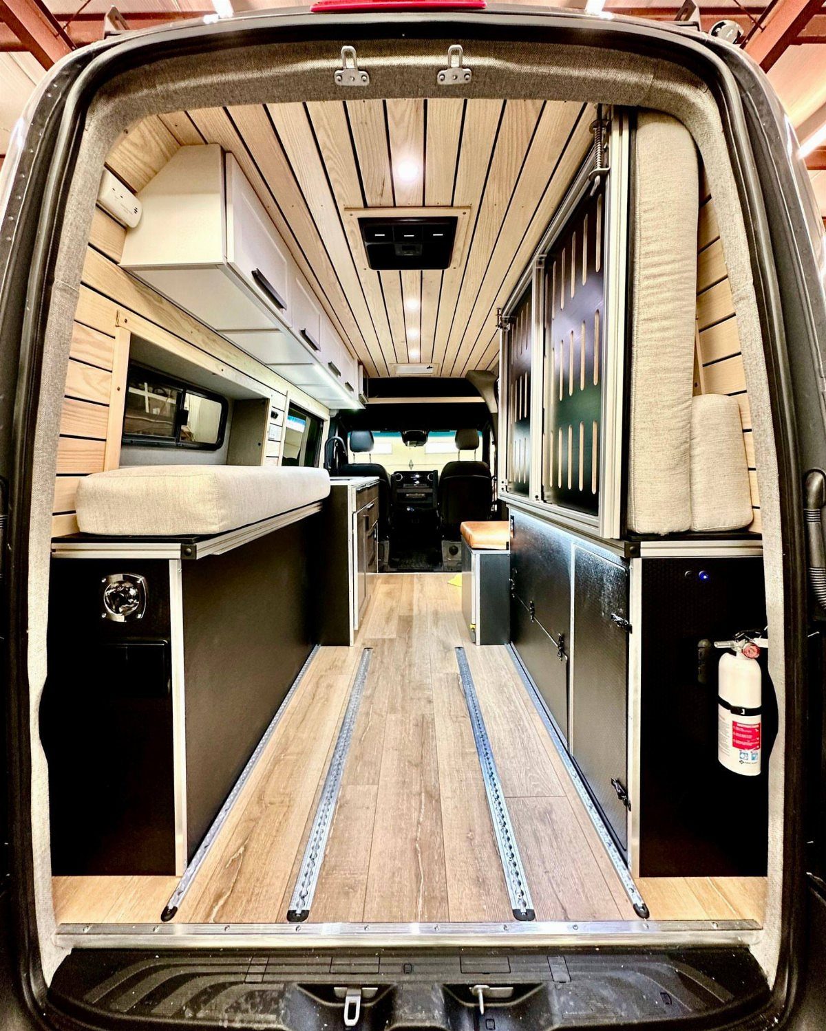 Converted van interior with a raised bed, wood paneling, and black storage cabinets.