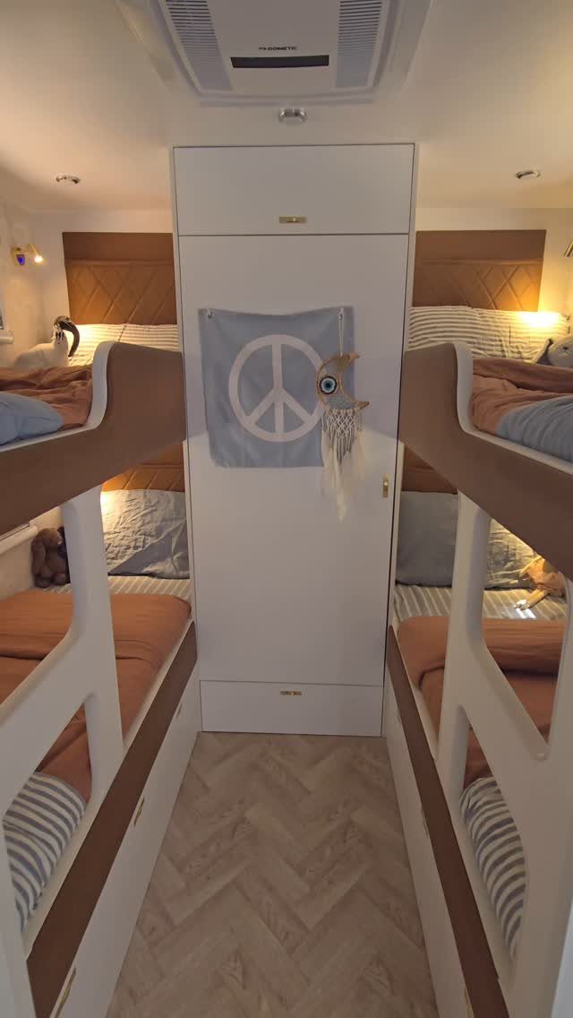 RV bedroom with bunk beds, white wardrobe, and light herringbone wood flooring.