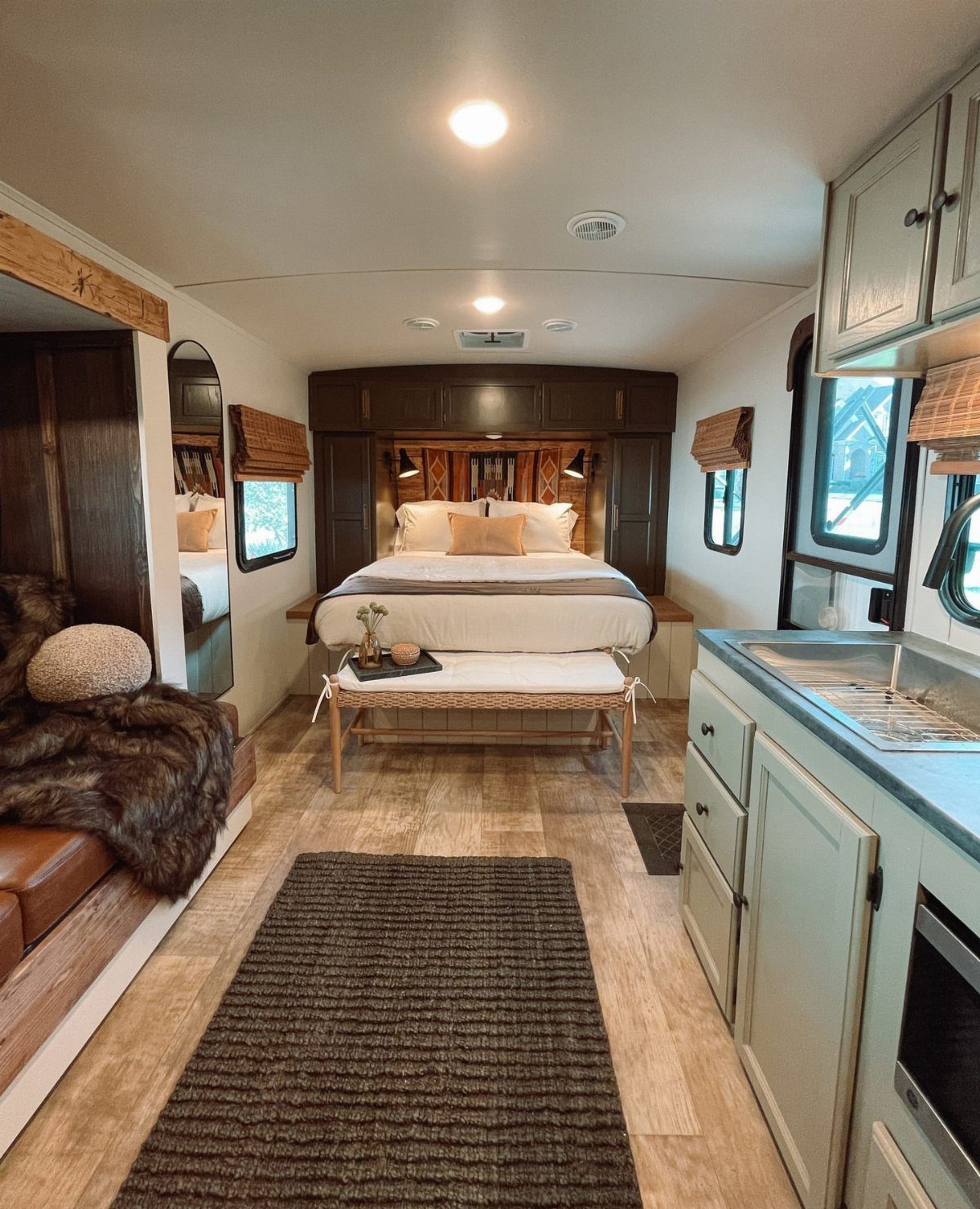 Remodeled RV bedroom with white bedding, light wood floors, and grey-green cabinetry.