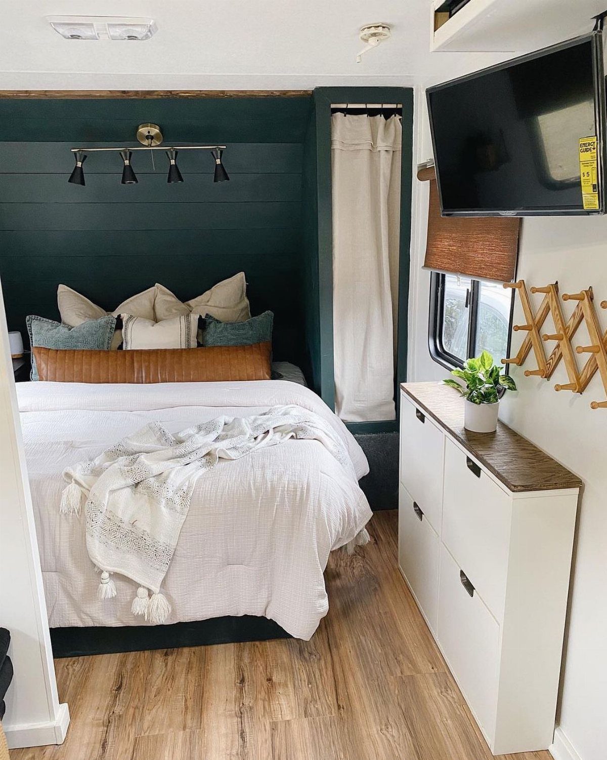 RV bedroom with a dark green wood accent wall and a white dresser.