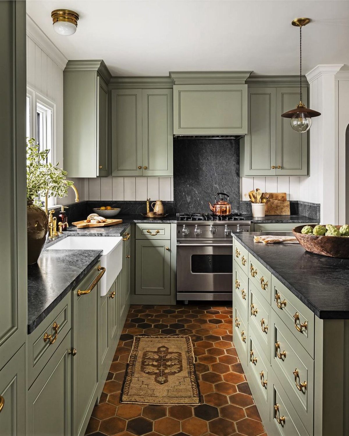26 Sage Green Kitchen Ideas Using Wood, Brass, and Marble 24 Sage green kitchen cabinets with black stone countertops and terracotta hexagonal floor tiles.
