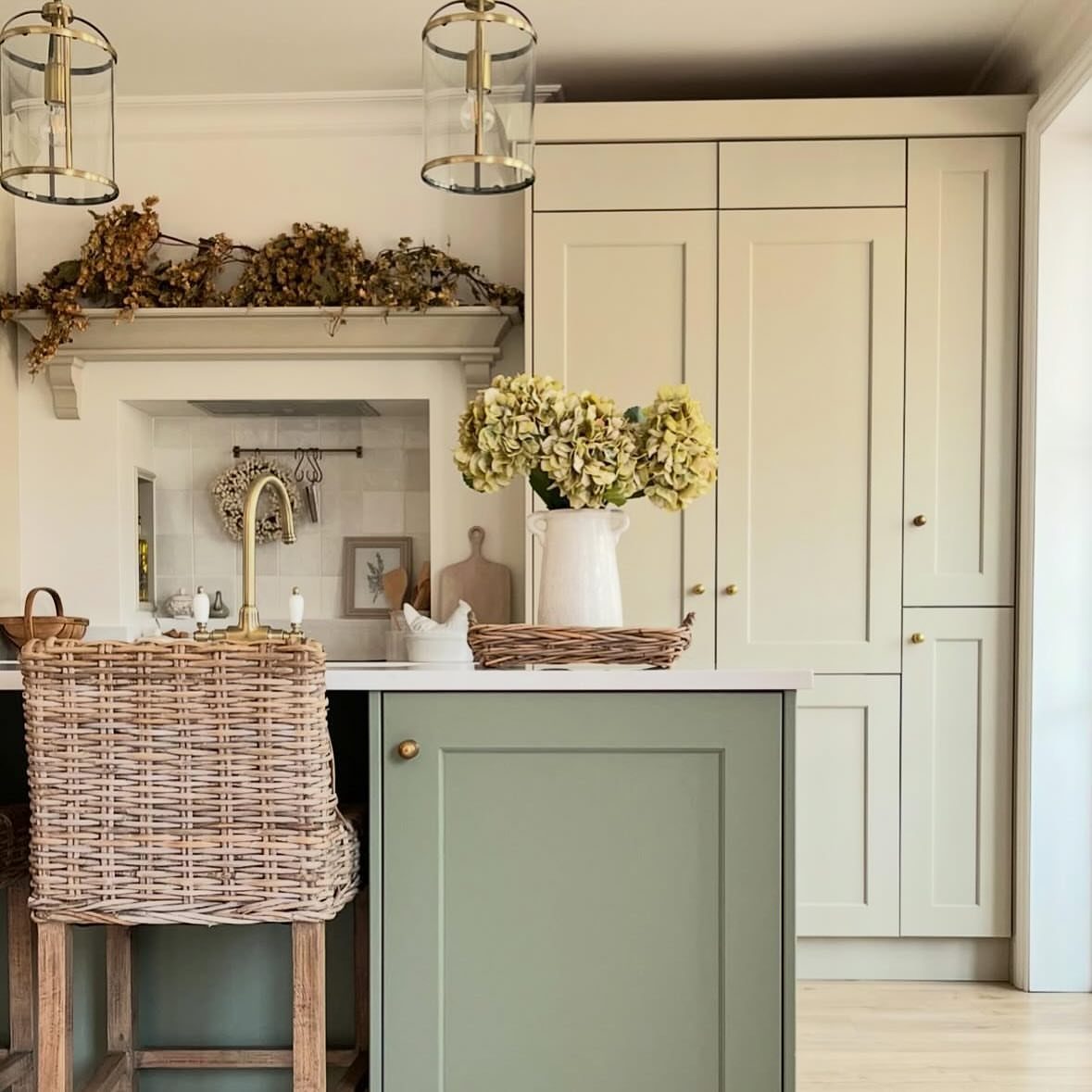 26 Sage Green Kitchen Ideas Using Wood, Brass, and Marble 10 Sage green kitchen island with cream cabinets, gold hardware, and a wicker stool.