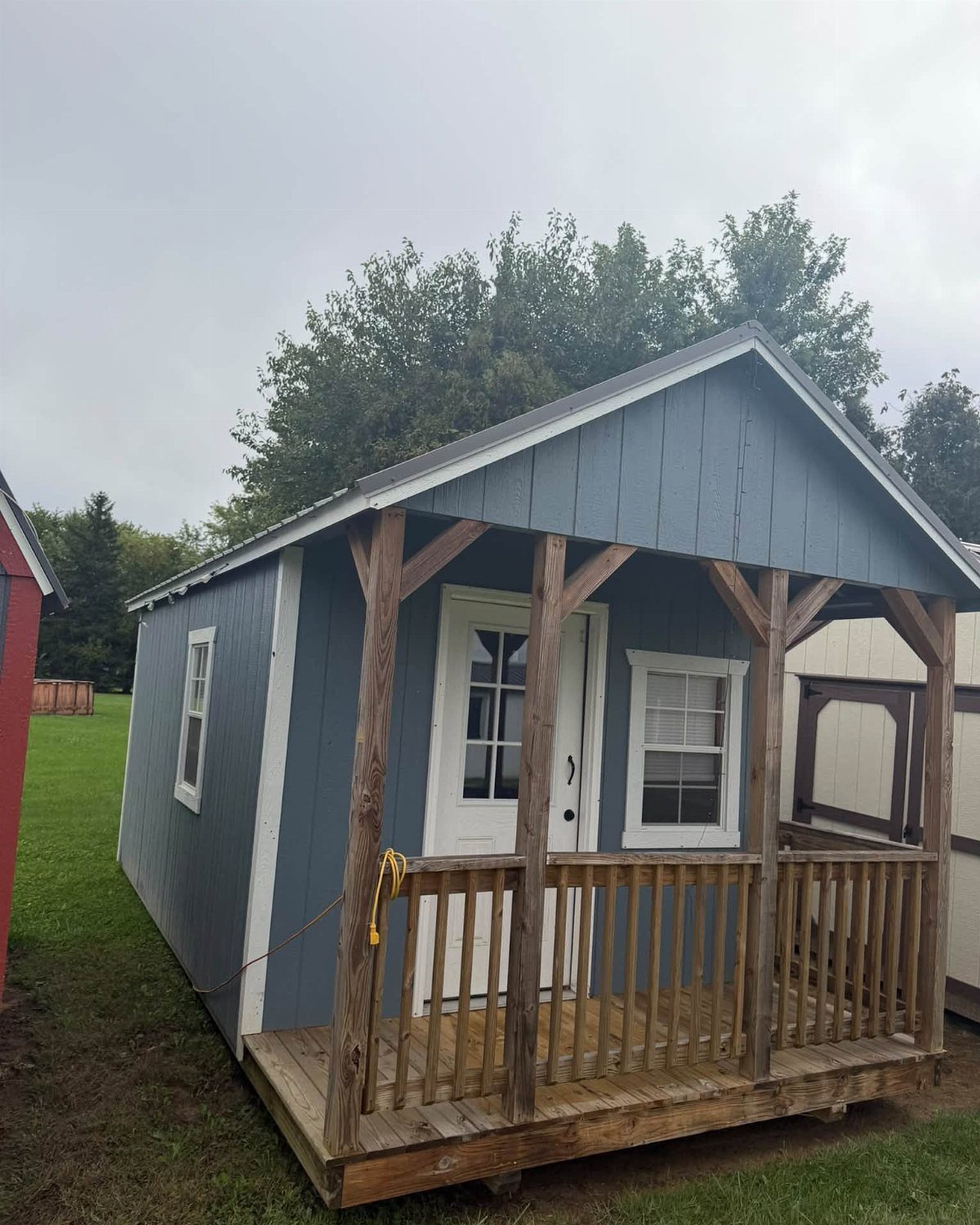 7 Shed with Porch Ideas for Storage, Studios and More 1 Blue wooden shed with a front porch, white door, and wooden railing.