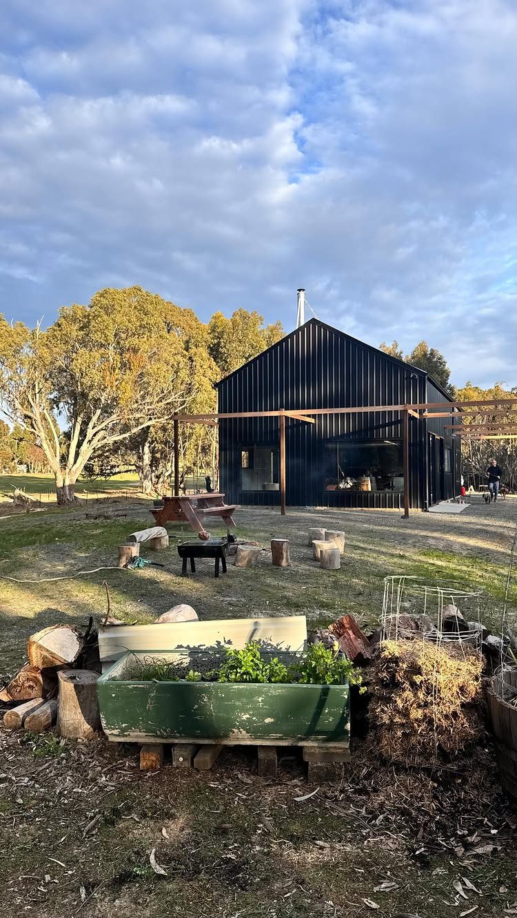 7 Shed with Porch Ideas for Storage, Studios and More 7 Black corrugated metal shed with a wooden porch frame in a grassy field.
