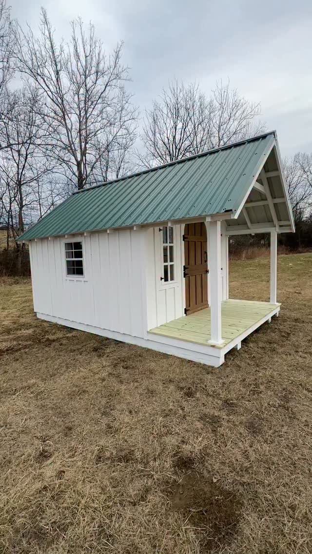 7 Shed with Porch Ideas for Storage, Studios and More 3 White wooden shed with a green metal roof and a small front porch.