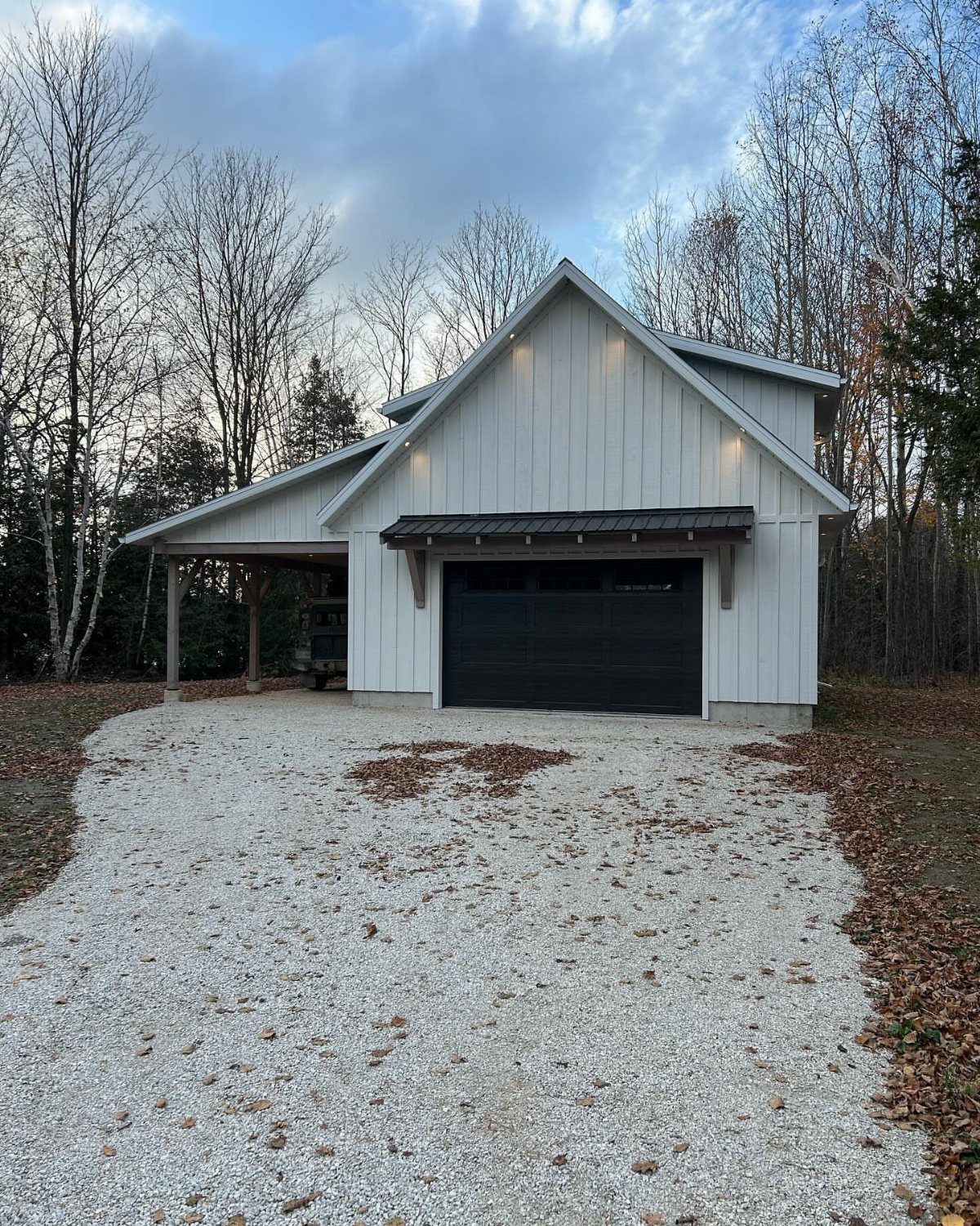 7 Shed with Porch Ideas for Storage, Studios and More 4 White barn shed with a black garage door and a side porch on gravel.