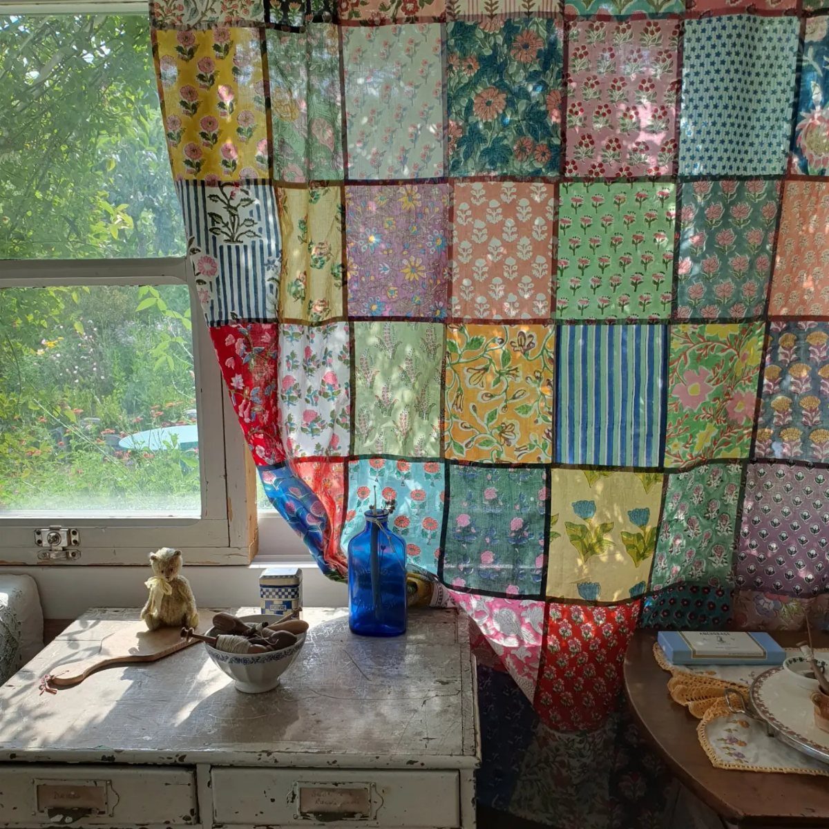 Patchwork fabric curtains hanging over a window above a white vintage dresser