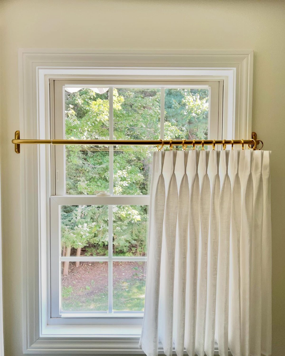 White short curtains on a gold rod hanging over a bright window
