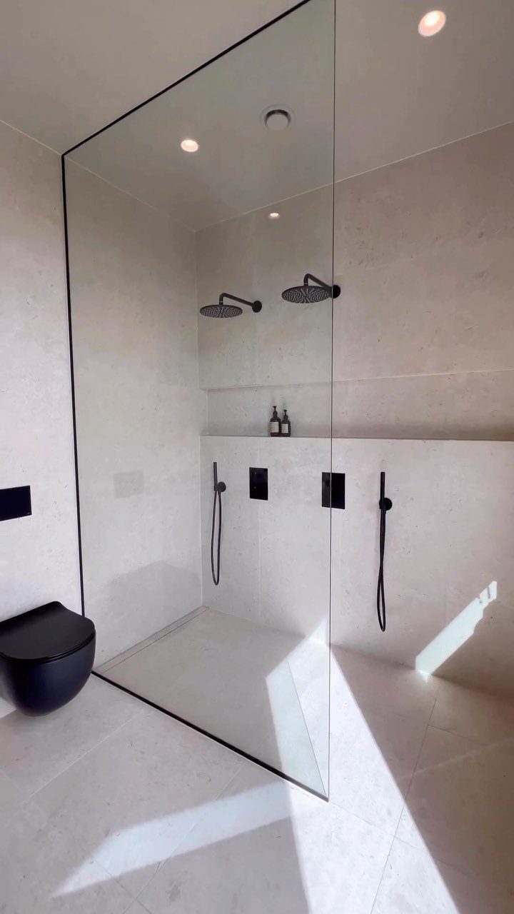 Curbless walk-in shower with glass partition and black fixtures in a white bathroom