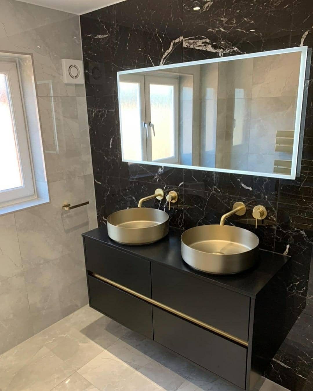 Wide rectangular mirror above double gold vessel sinks on a black floating vanity.