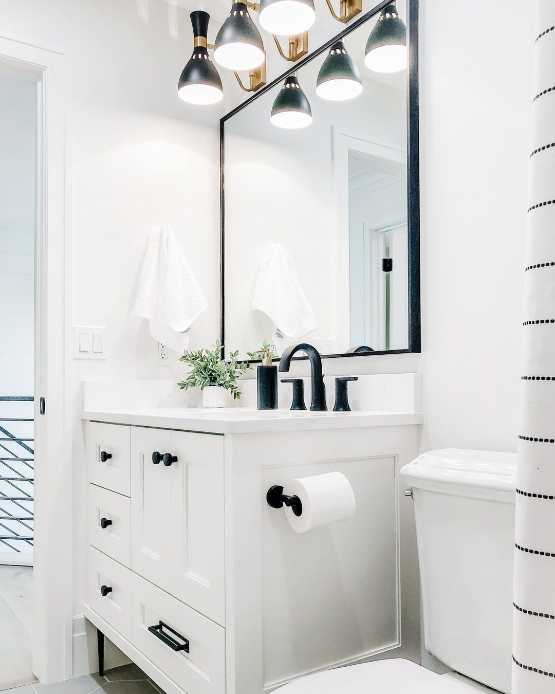 White bathroom vanity and toilet in a bright room with black accents.