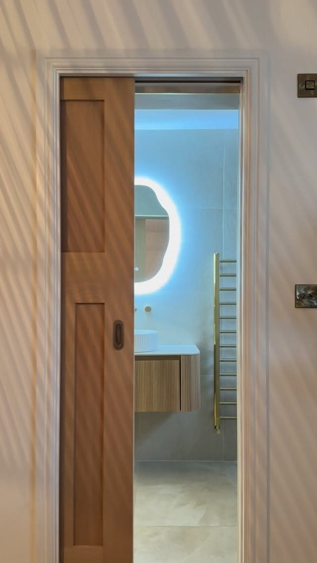 Wooden pocket door partially open leading into a modern, bright master bathroom.