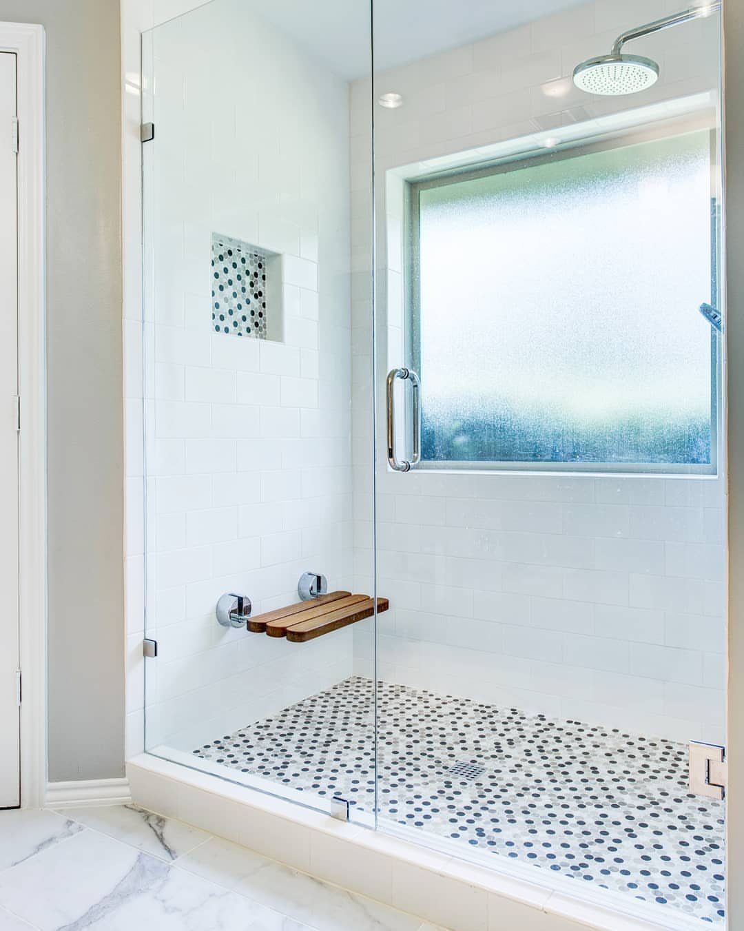 Wooden floating shower bench in a white tiled walk-in shower with glass doors.