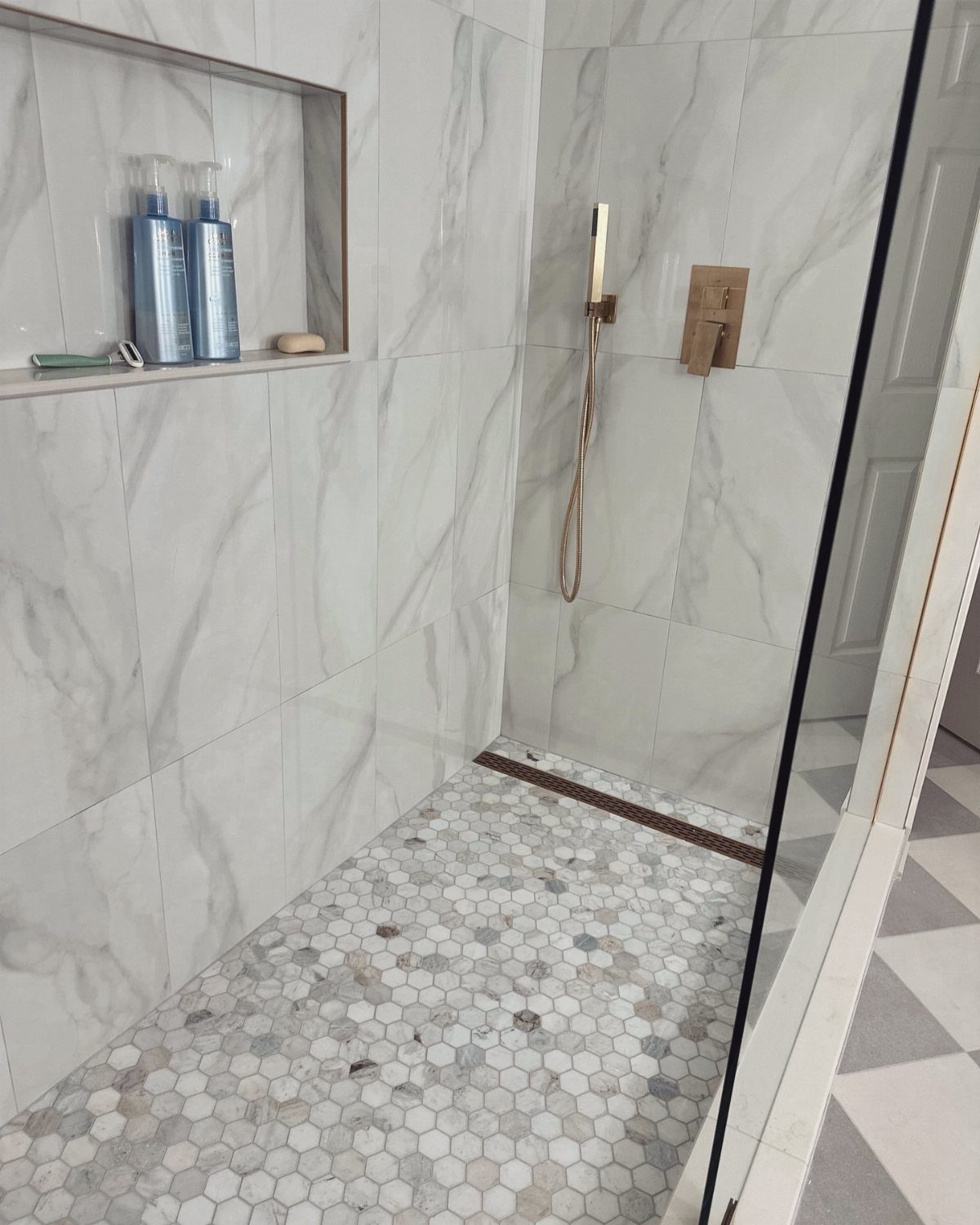 Walk-in shower featuring white marble walls and grey and white hexagonal floor tiles.