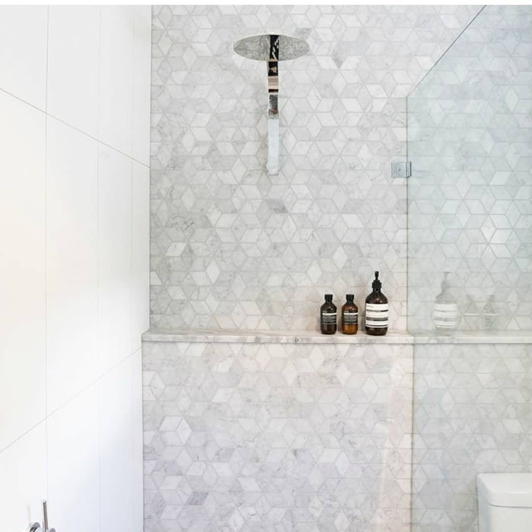 Marble shower with hexagonal tiles and a built-in ledge holding soap bottles.