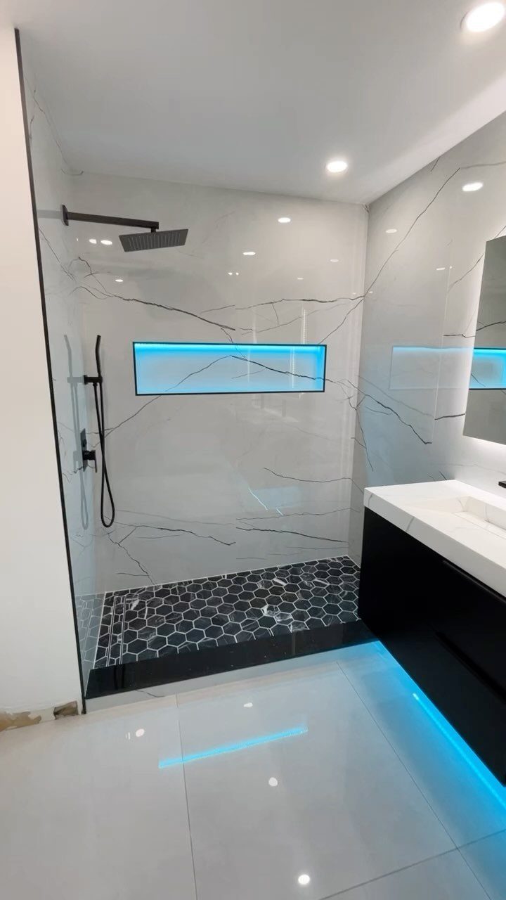 Modern walk-in shower with white marble walls and a blue illuminated recessed shower niche.