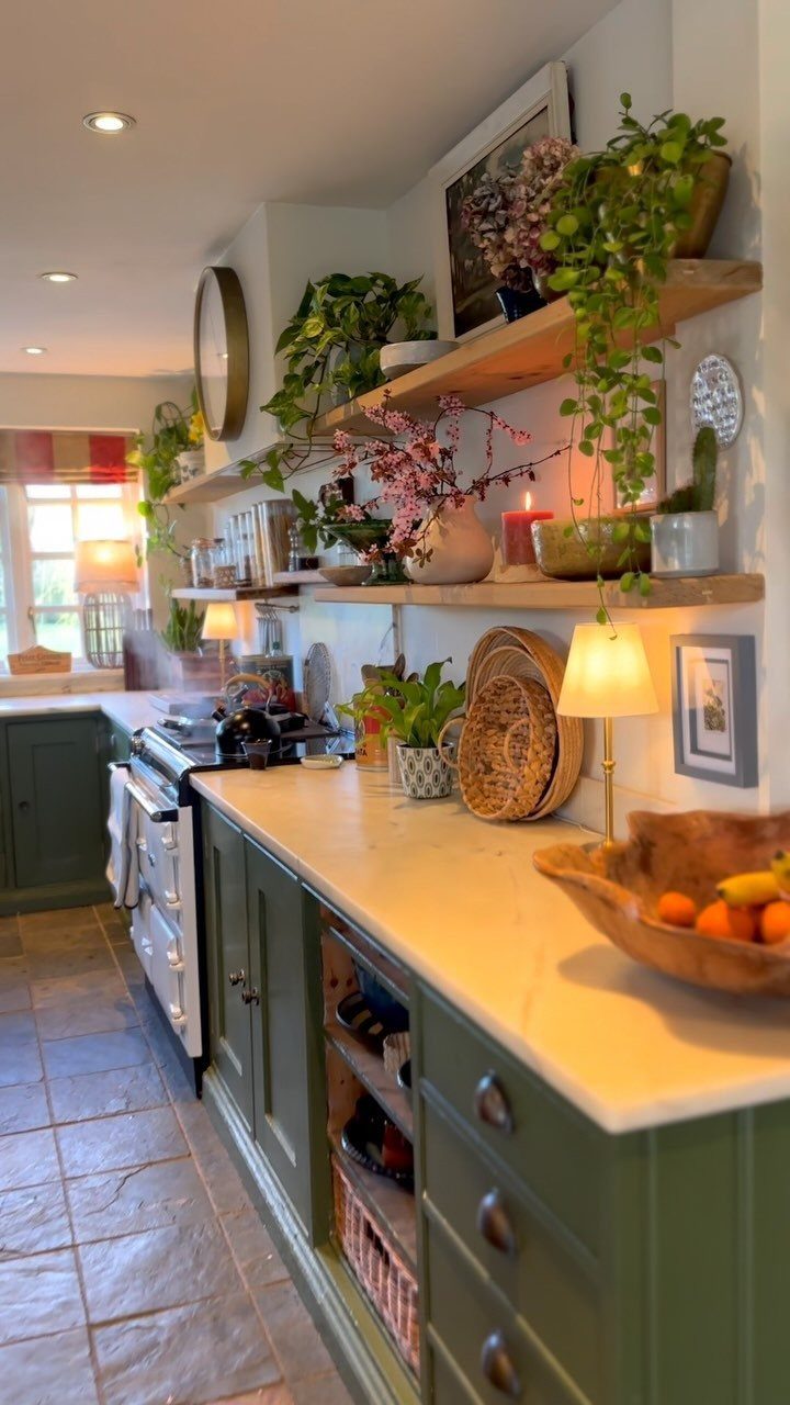 UK Kitchen Ideas Green: 21 Cabinet, Tile and Worktop Looks 20 Sage green kitchen cabinets with white countertops and wooden shelves holding trailing plants.