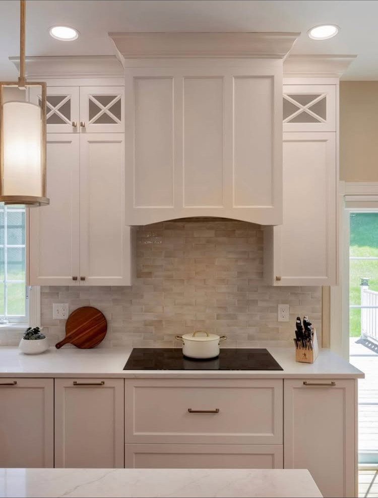 Cream shaker cabinets with crown molding and a light tiled backsplash in a kitchen.