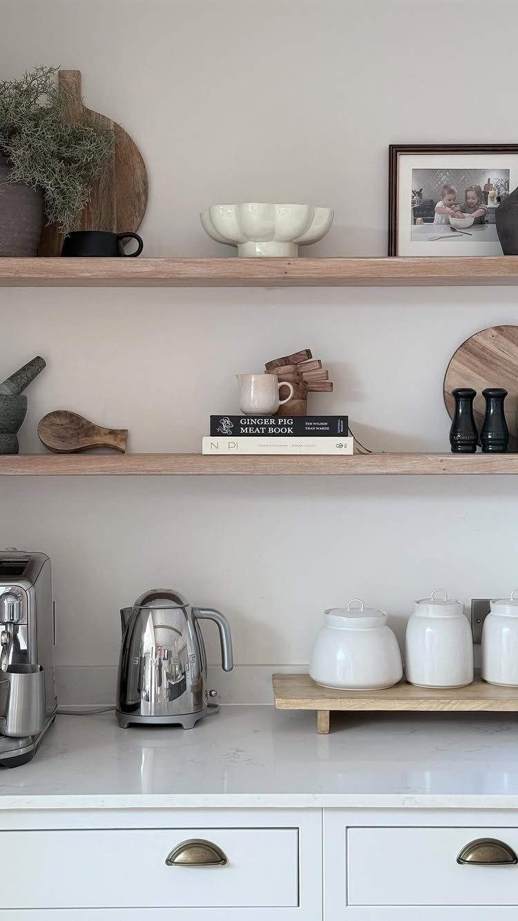 Light wood open shelving with kitchenware above white cabinets and a white countertop.
