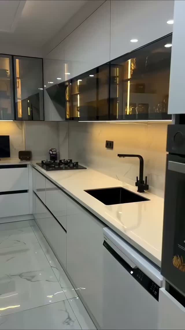 Modern white kitchen with contrasting dark glass upper cabinets and black hardware.