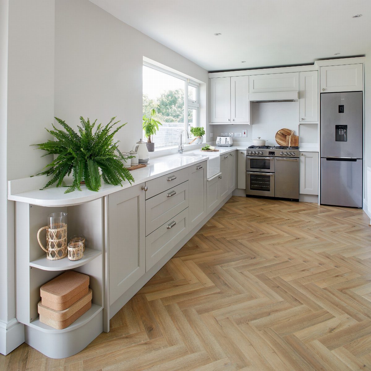 Light cream kitchen cabinets with light wood herringbone flooring and white countertops.