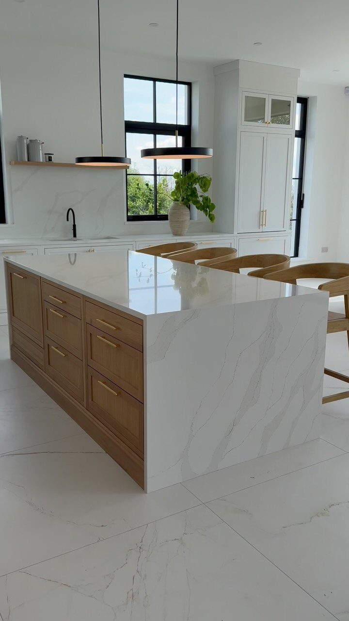 Kitchen island with light wood cabinets and white marble waterfall countertop in bright room.