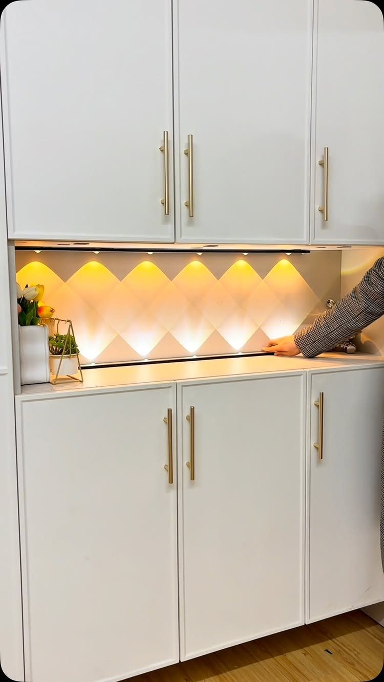 White kitchen cabinets with gold hardware and warm under-cabinet lighting over a textured backsplash.