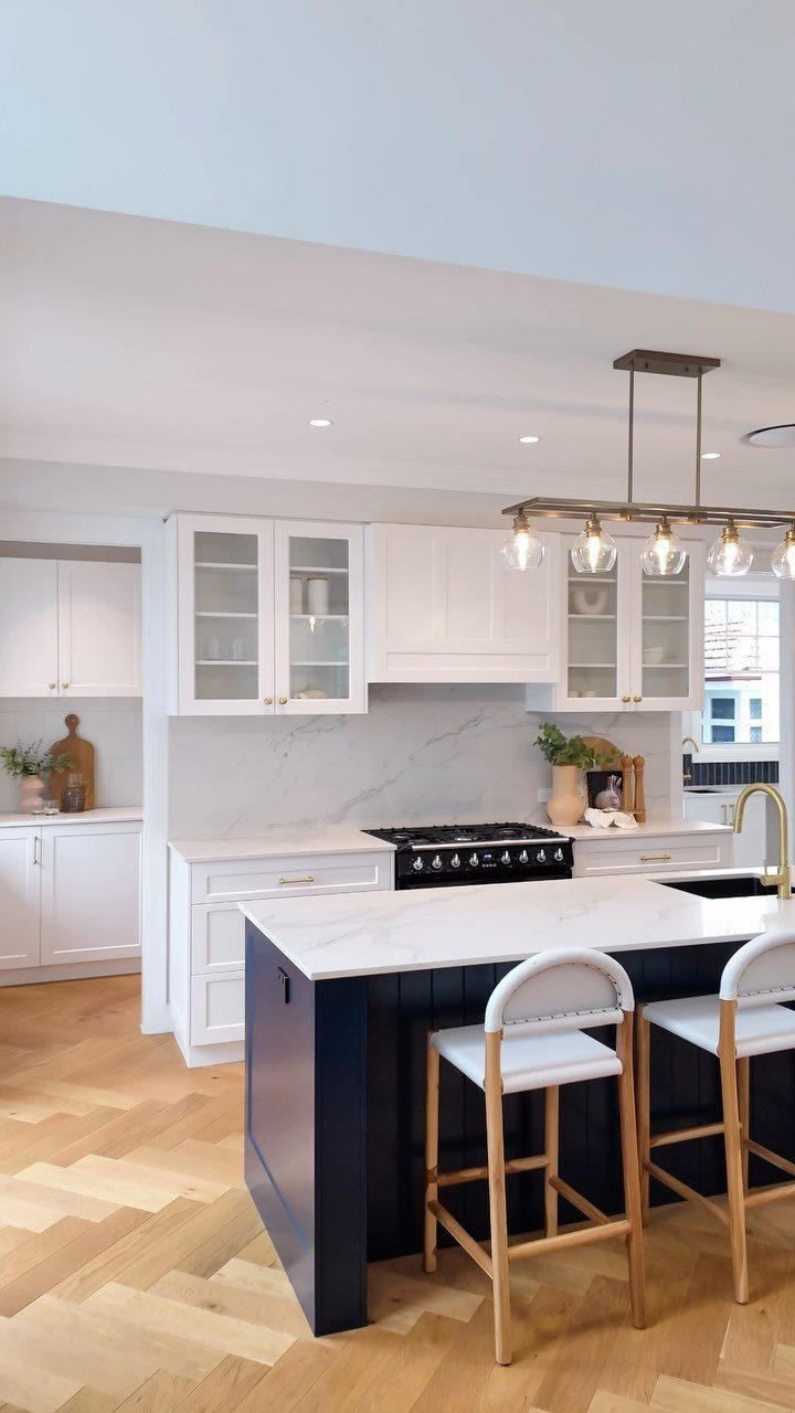 Navy blue kitchen island with white marble top and cream shaker cabinets.